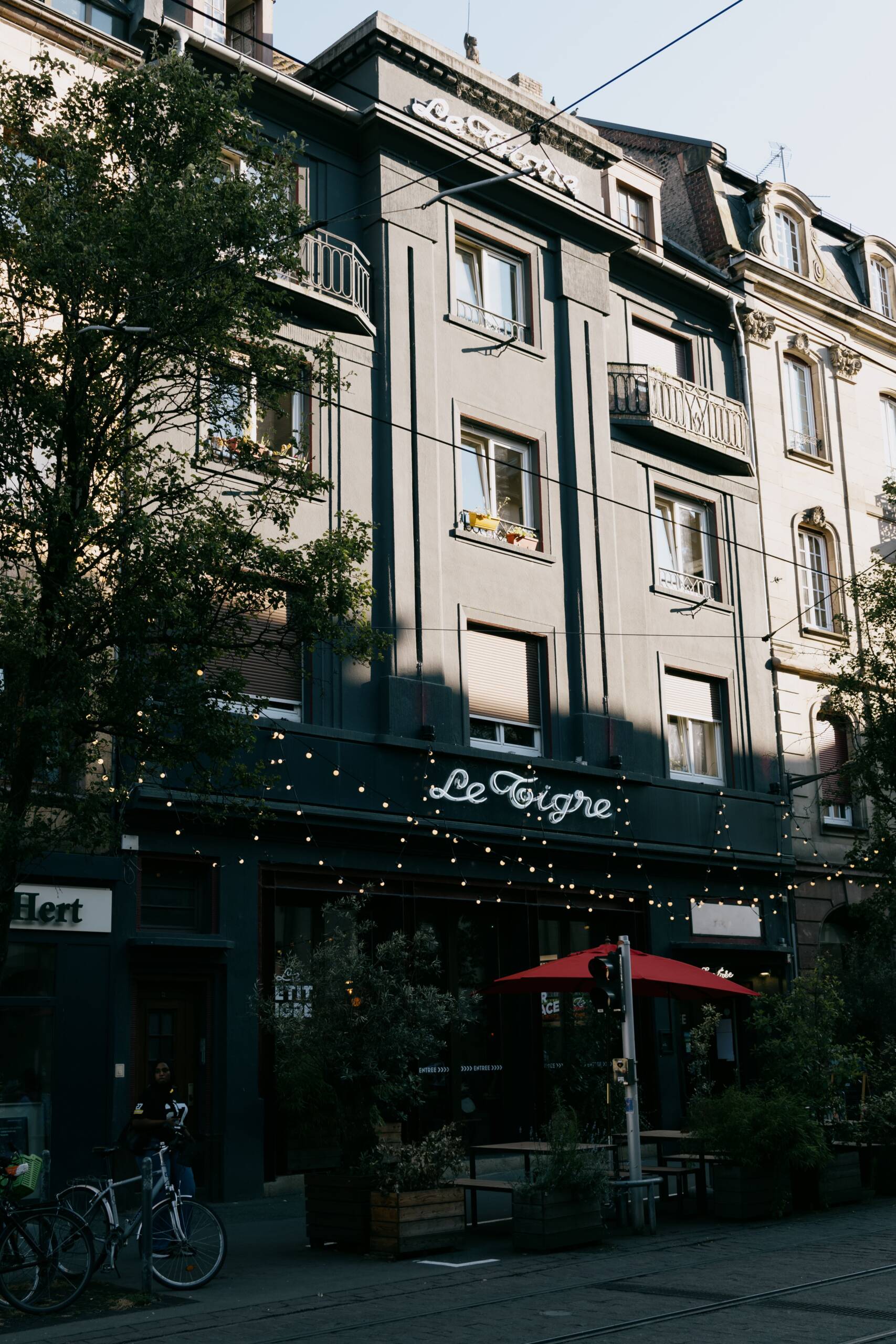 Vue de la façade du Bar Le Petit Tigre à Strasbourg, avec la terrasse et son parasol rouge, sous les guirlandes lumineuses, Rue du Faubourg National.