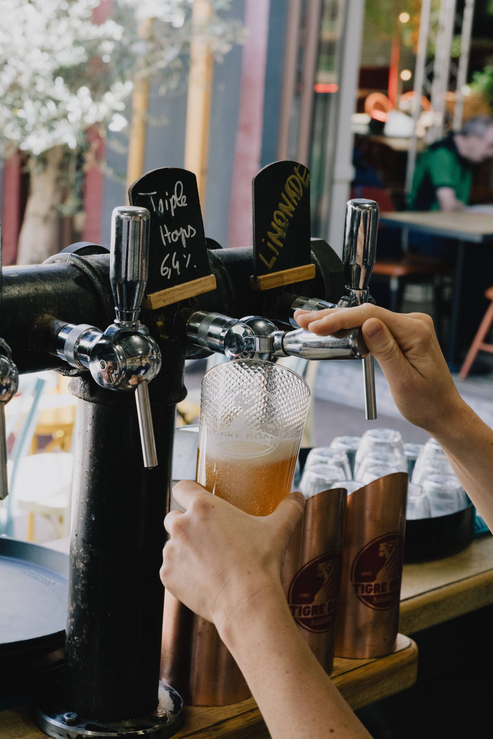 Mains d'un barman tirant une bière de type "Triple Hops" à partir d'un robinet de la brasserie Le Tigre. Le verre porte le logo de la brasserie.